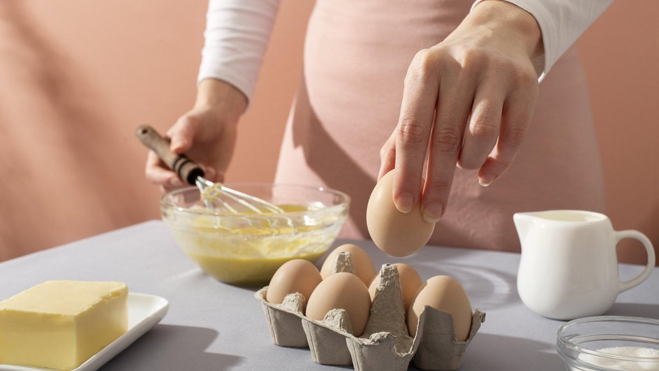 Женщина в розовом фартуке взбивает куриные яйца, чтобы проверить себя на болезнь Паркинсона 